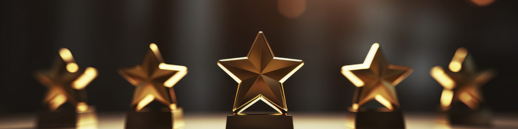 A close-up of golden star trophies arranged on a table, illuminated by soft lighting.
